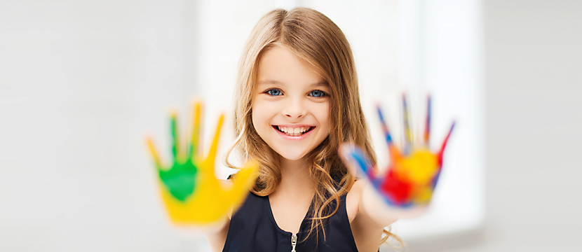 A pre-teen girl smiling and holding out her outstetched palms covered in colourful paint