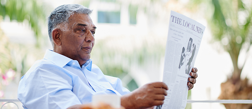 A middle-aged man seated outdoors and reading a newspaper