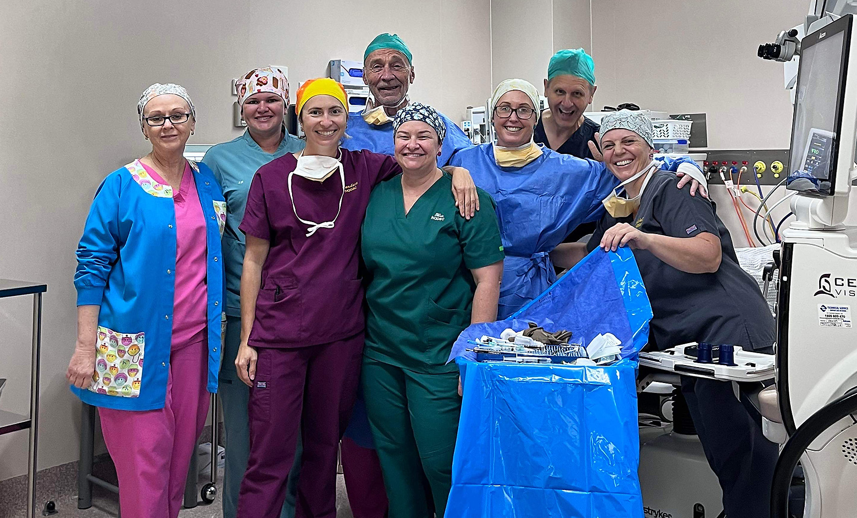 People in scrubs standing together in an operating theatre and smiling at the camera.