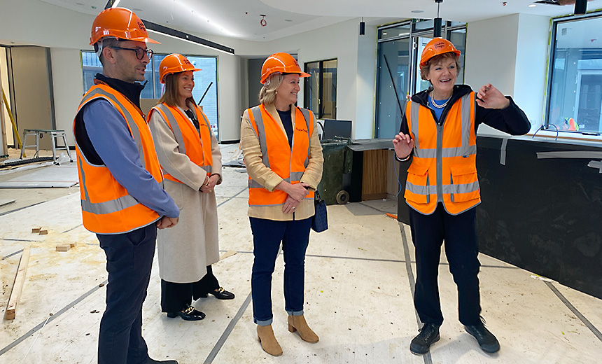 Dr Russell Harrison, Amanda Cranage and Siobhan Todhunter stand together with a guide giving them a tour of the redevelopment site. Everyone is wearing orange safety vests and orange hard hats.