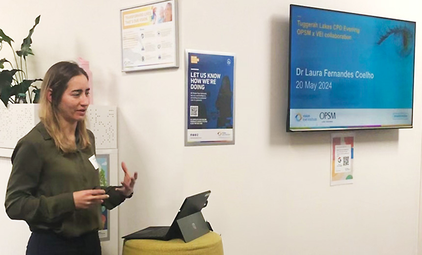 Dr Laura Fernandes Coelho stands presenting at a podium in Vision Eye Institute's Tuggerah Lakes clinic. Nearby is a projector showing a Powerpoint slide reading, 'Tuggerah Lakes CPD Evening, OPSM x VEI collaboration, Dr Laura Fernandes Coelho, 20 May 2024." It has the Vision Eye Institute and OPSM logos at the bottom of the screen.