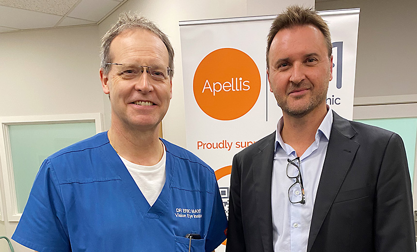 Dr Eric Mayer wearing blue scrubs and smiling at the camera, standing next to the representative from Apellis, the sponsor of the CPD event at Box Hill, VIC.