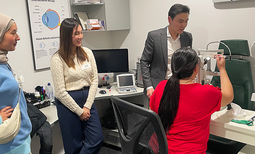 Dr Tiger Zhou supervises as an optometrist views a model eye through diagnostic equipment at the Specsavers West Lakes event. Two other optometrists observe.