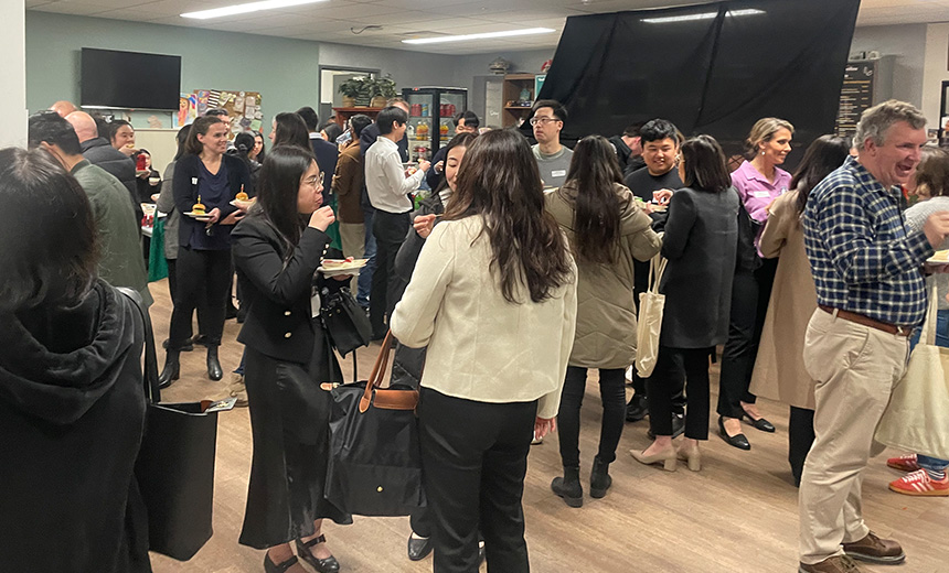 A photo of a restaurant filled with people. The tables and chairs have been moved out of shot and the people are all standing and talking in small clusters. Most people are holding plastic plates filled with food.