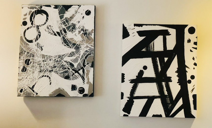 Two of Dr Rushmia Karim's abstract artworks in black, white and grey hanging side by side on a wall.