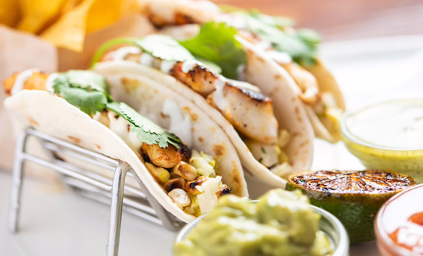 A photo of three fish tacos on a plate with some salsa and guacamole on the side.