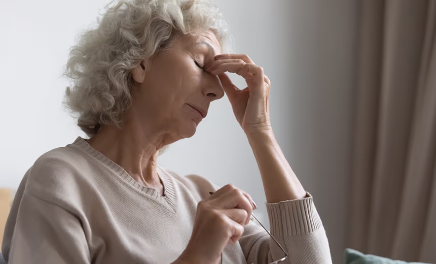 An older woman pinching the bridge of her nose while her eyes are closed.