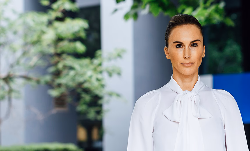 Outdoor headshot of ophthalmologist Dr Abi Tenen in a white blouse. She is standing in front of the Melbourne clinic with the building and trees softly blurred in the background.