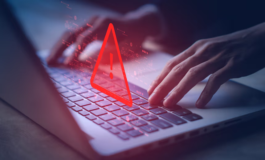 Close-up of hands typing on a laptop computer, the light is dim and a holographic version of the screen floats in front of the hands with red glowing diagrams and code and a large red ‘alert’ triangle with an exclamation mark within it.