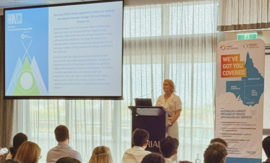 VEI CEO, Amanda Cranage's welcome address. She is standing in front of a crowd, positioned behind a lectern with a microphone. A projector screen is positioned to the left of the image. VEI signage is positioned to the right of the image.