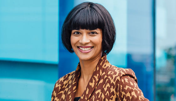 Dr Christolyn Raj dressed in an animal print dress standing outside a building with mirrored windows