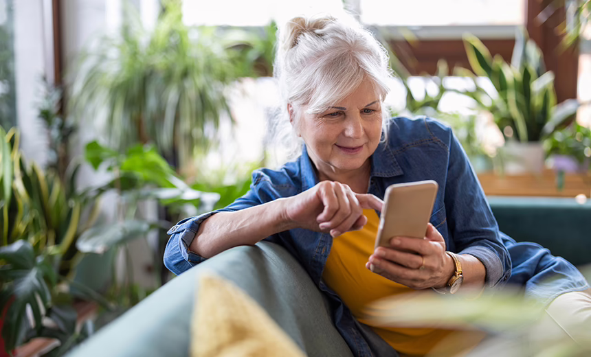 An older woman sitting on a couch while using a smartphone.