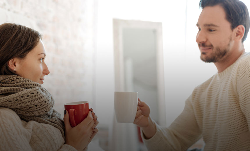 Young man and woman each holding a hot drink in a cosy living area