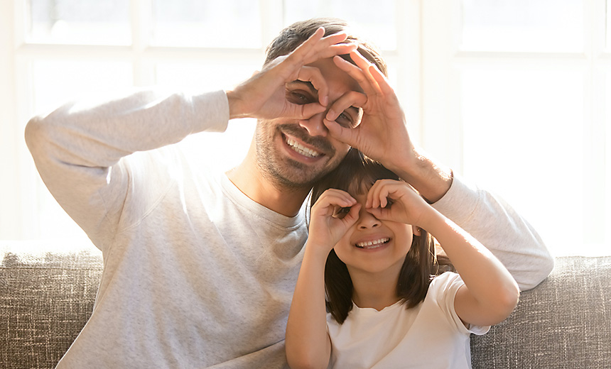 Pretty family father adorable daughter sitting on sofa do funny faces making with fingers eyewear shape like glasses looking through binoculars, have fun with child free time play tricks fool concept (Pretty family father adorable daughter sitting on