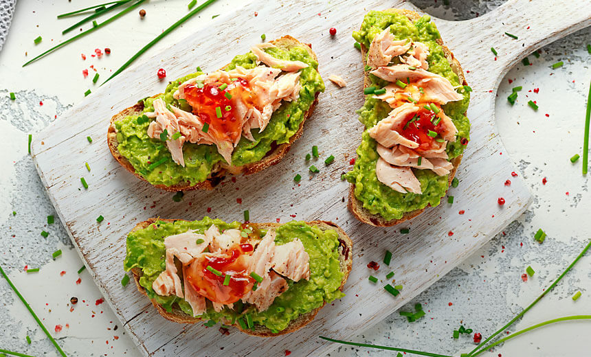 Slices of toast with avocado, cooked salmon, leafy greens and red onion garnish