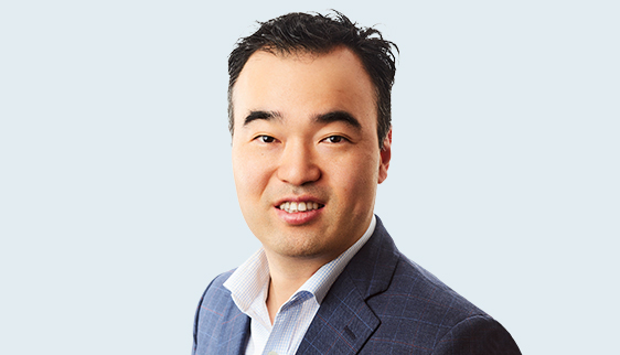 Headshot (shoulders upwards) of Dr Peter Kim a young Asian man with short black hair. Dr Kim is wearing a navy blue blazer and light blue collared shirt with the first button undone