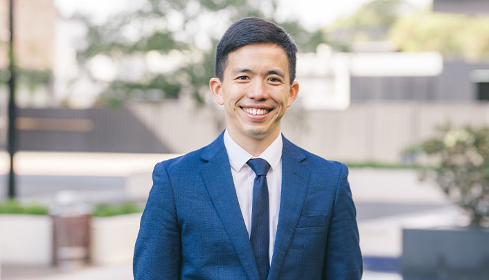 Outdoor portrait shot of Dr Christopher Go in a dark blue suit jacket over a pale blue, collared shirt and dark blue tie