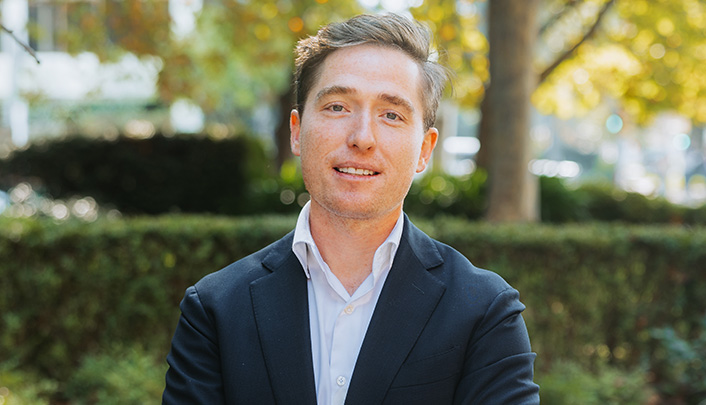 Headshot of Dr Jack Kane in a dark blue suit and open-collared, white shirt outside Vision Eye Institute Melbourne